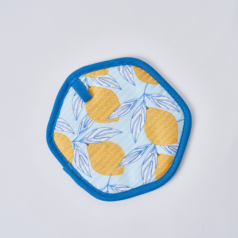 The Lots of Lemons Pot Holder is a stylish, heat-resistant hexagonal fabric coaster with a blue border, adorned with yellow lemons and blue leaves on a light blue background.